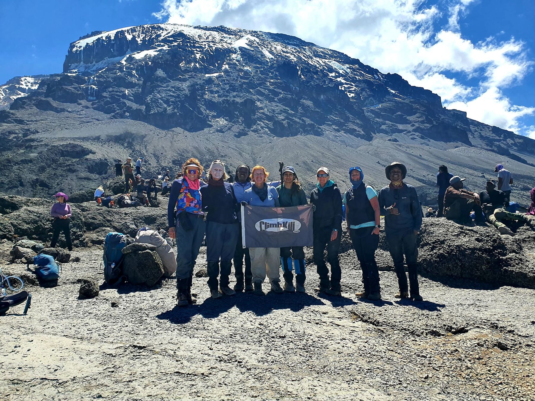 A group of women holding the Climb Kili flag with Kilimanjaro's snowy summit behind them