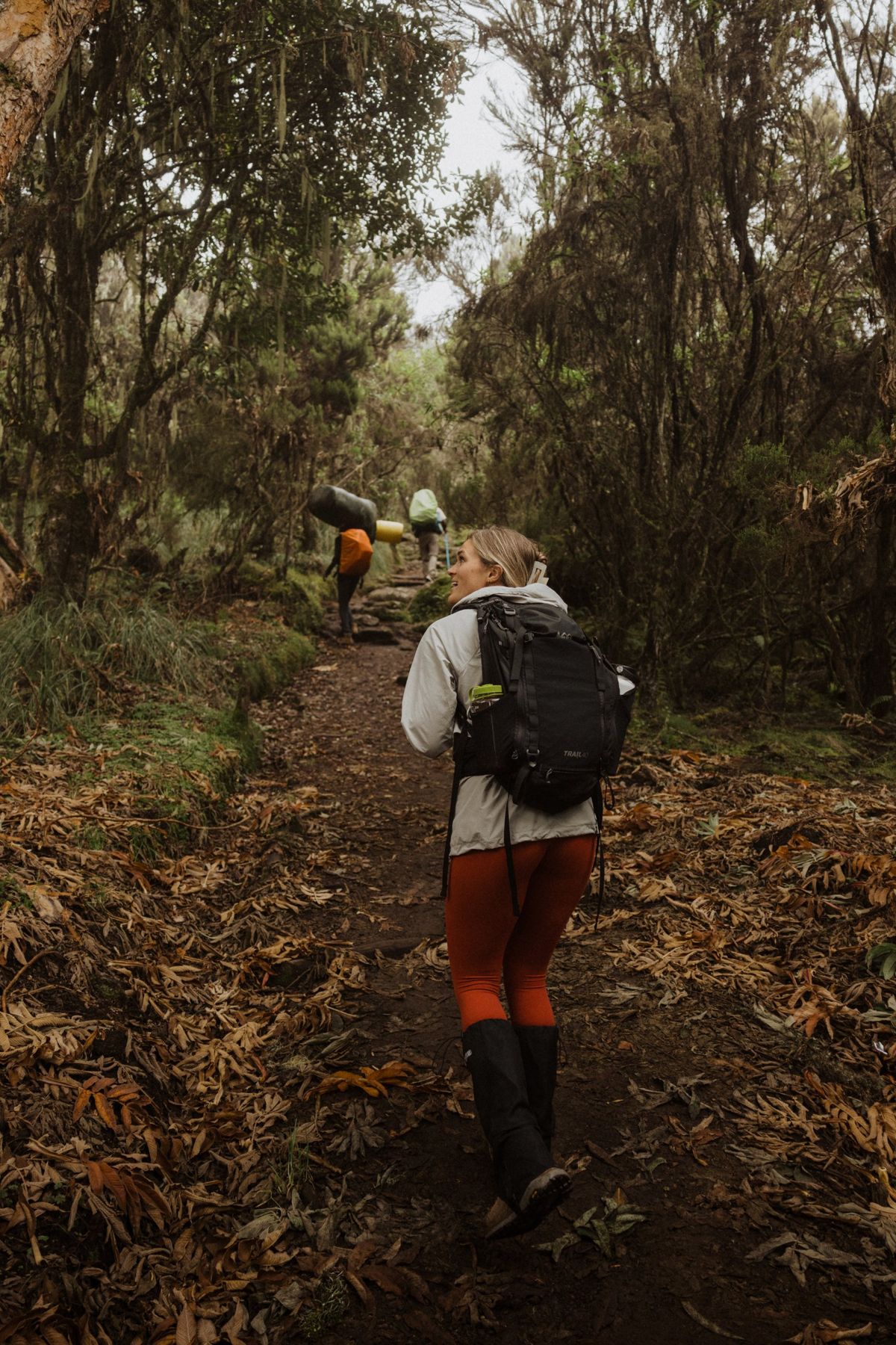 A smiling climber looking back on the rainforest trail as porters walk ahead
